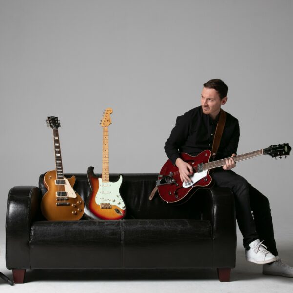 Roman Spilek auf einem Sofa mit seinen Gitarren